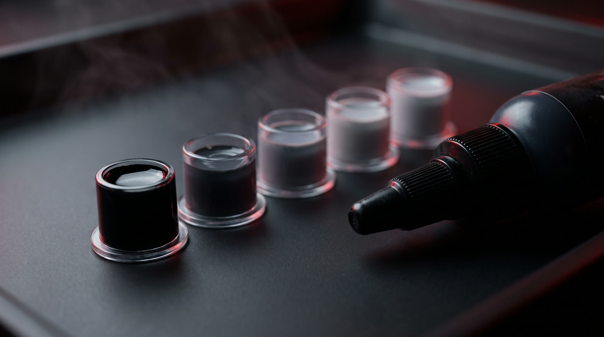 A row of ink caps holding a greywash scale from pure black to pale silver, under red neon