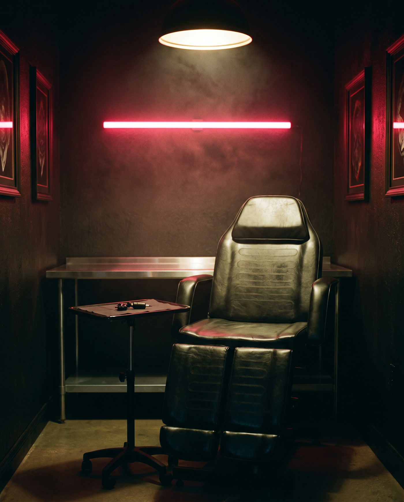 The studio: an empty tattoo chair under a warm light, steel workstation, and red neon on the wall